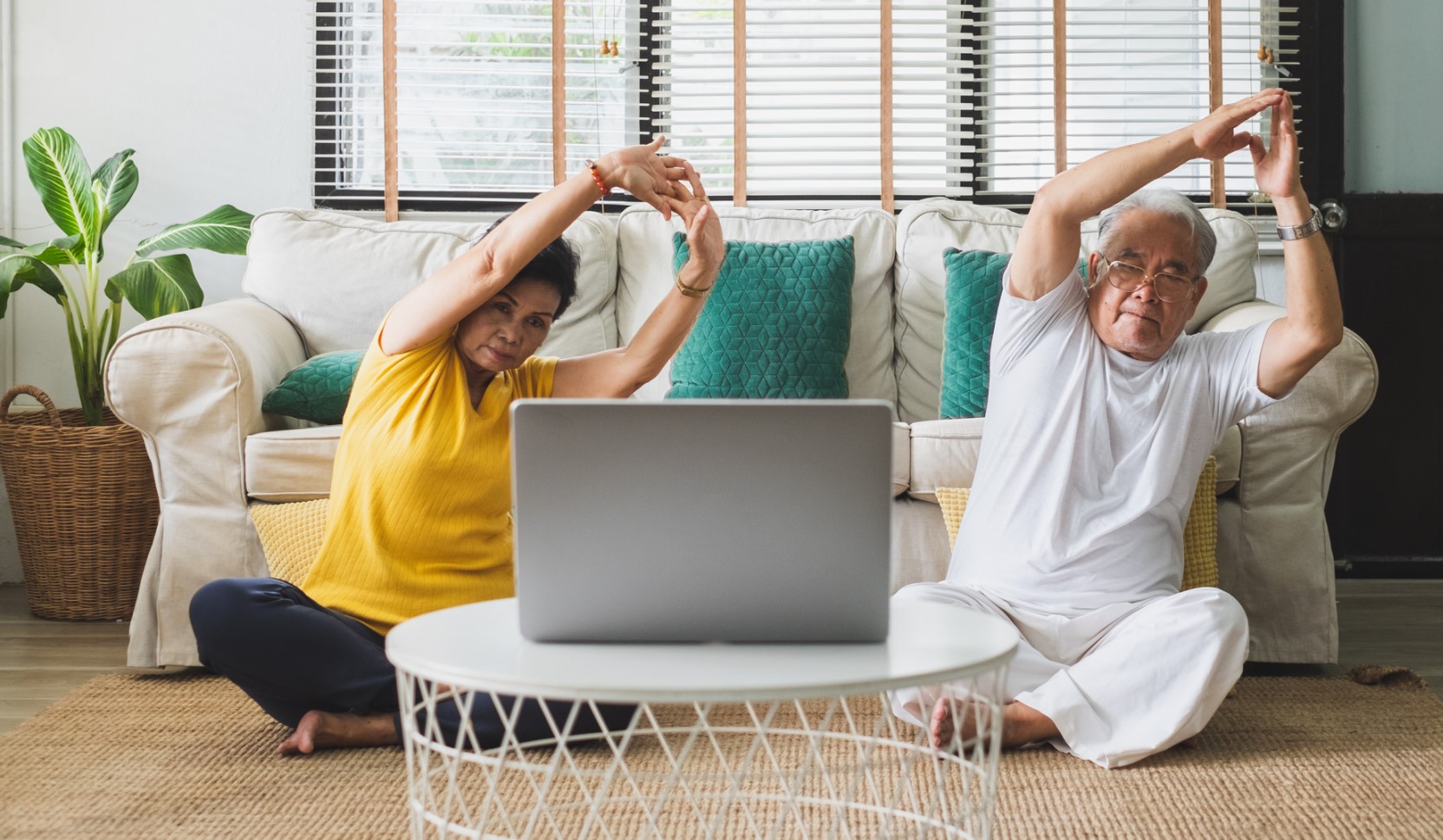 Senior Asian couple engaging in yoga on their living room floor.