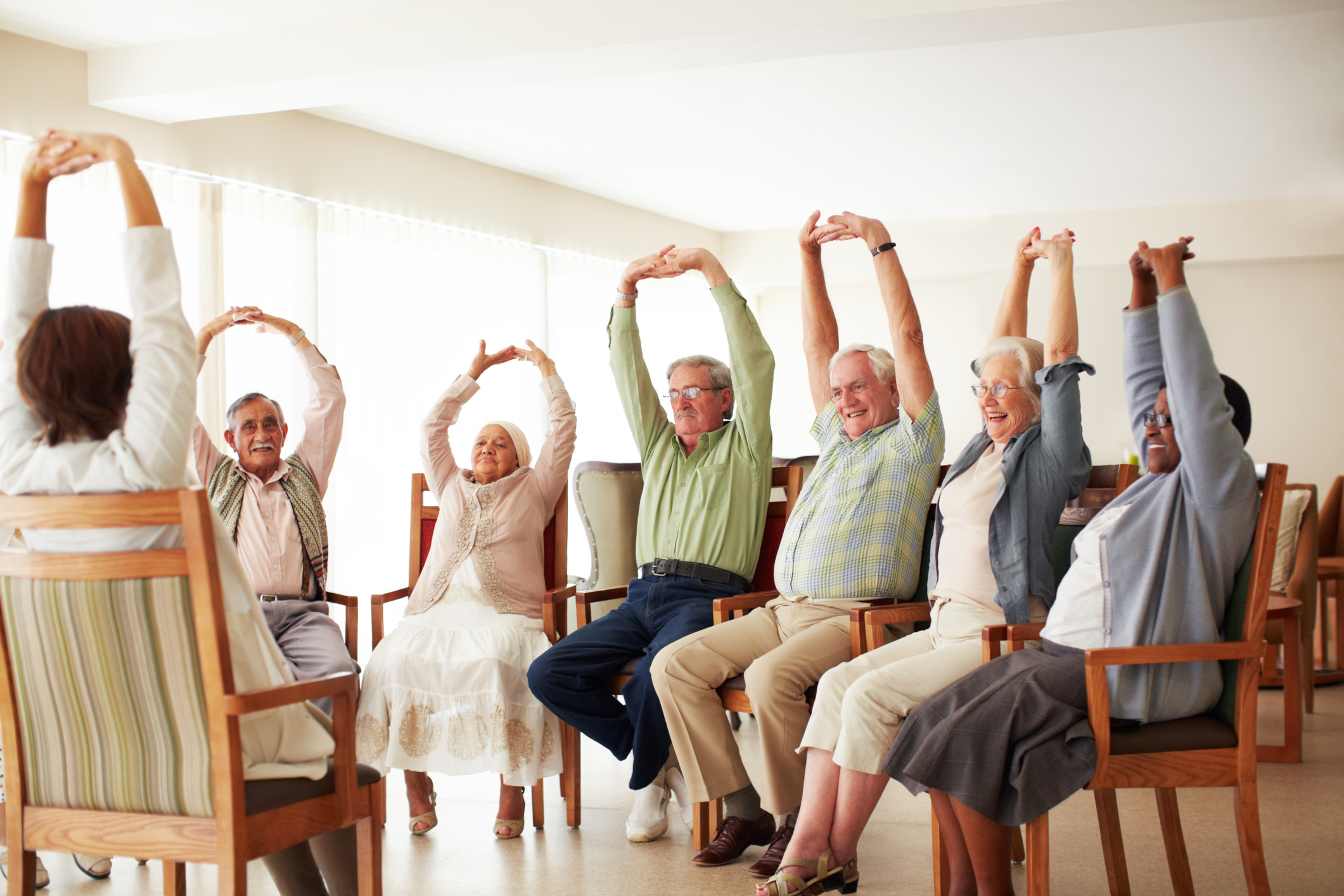 A gathering of individuals seated in chairs, engaged in an exercise session.