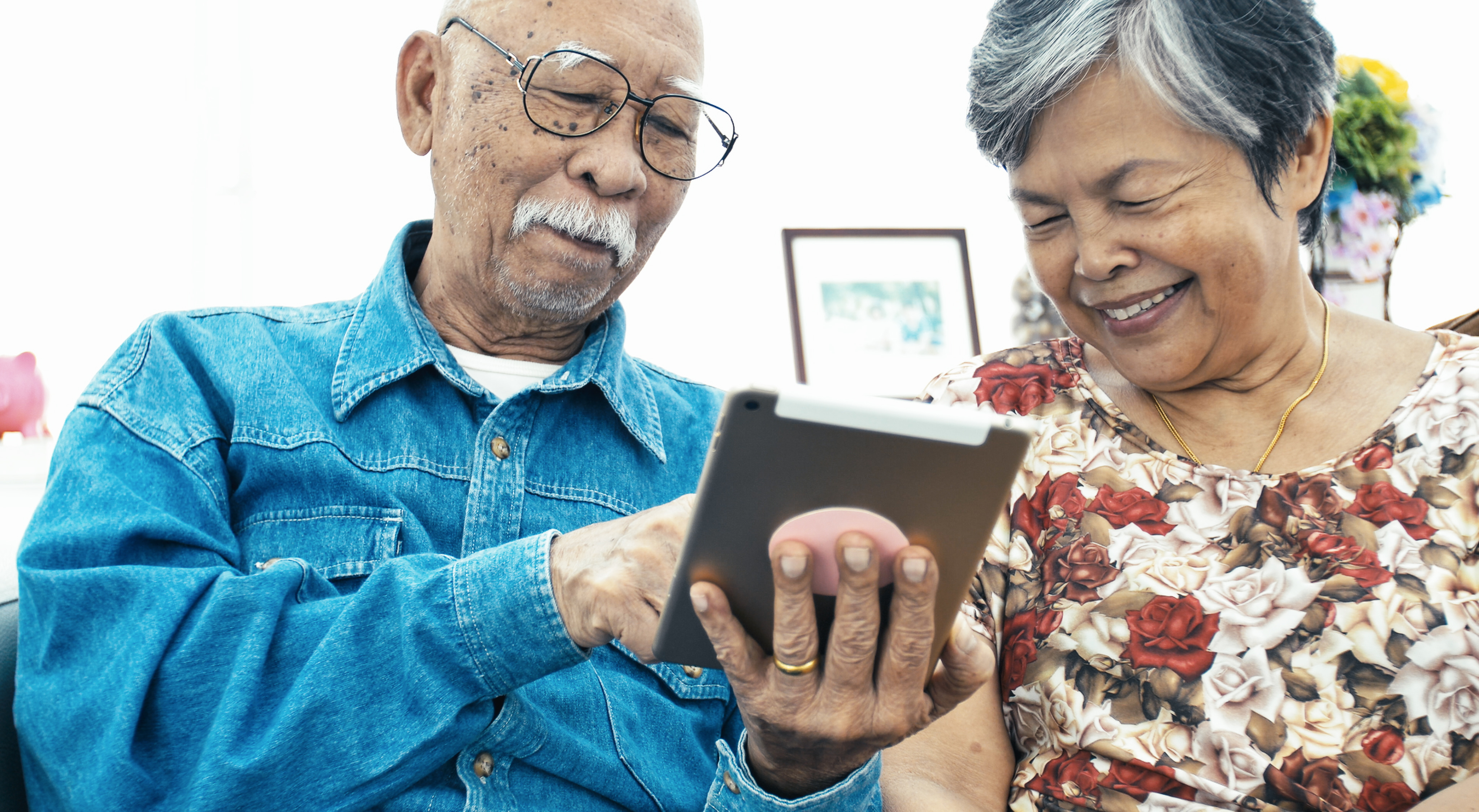 Two older adults smiling and using a tablet smart device