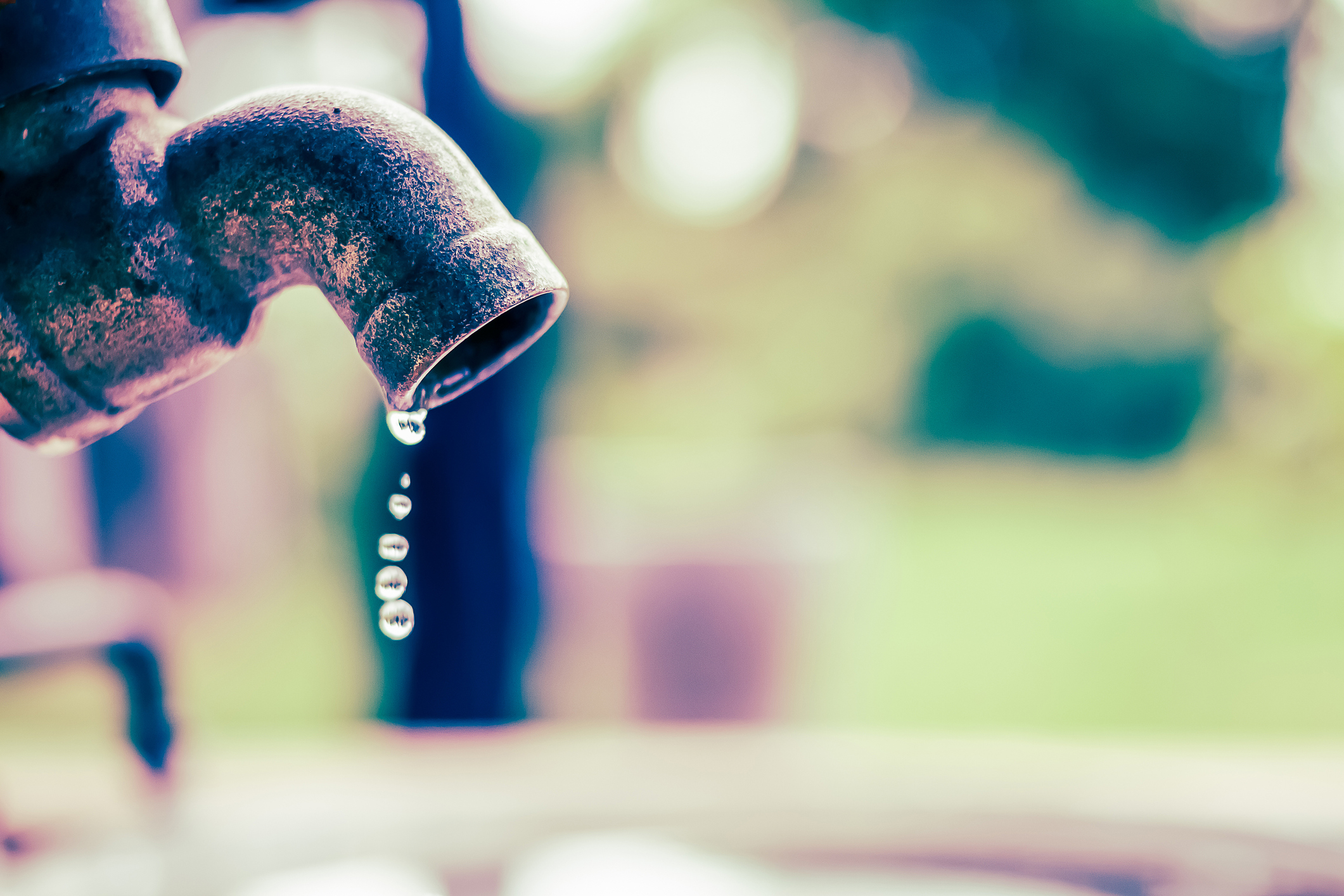 Close up image of a rusted metal water faucet with a few drops of water falling from the spout