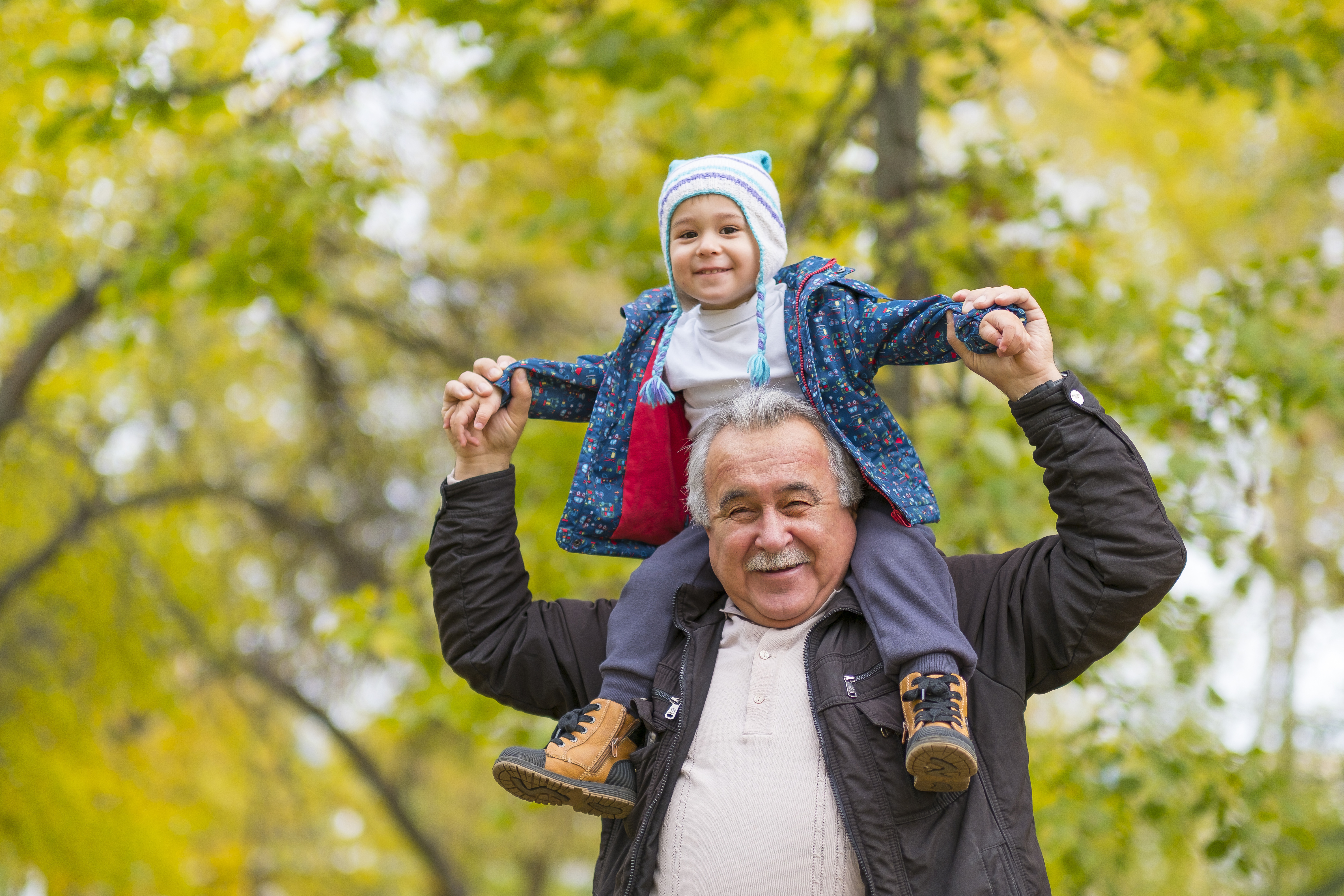 older adult man with toddler sitting on his shoulders, both are smiling