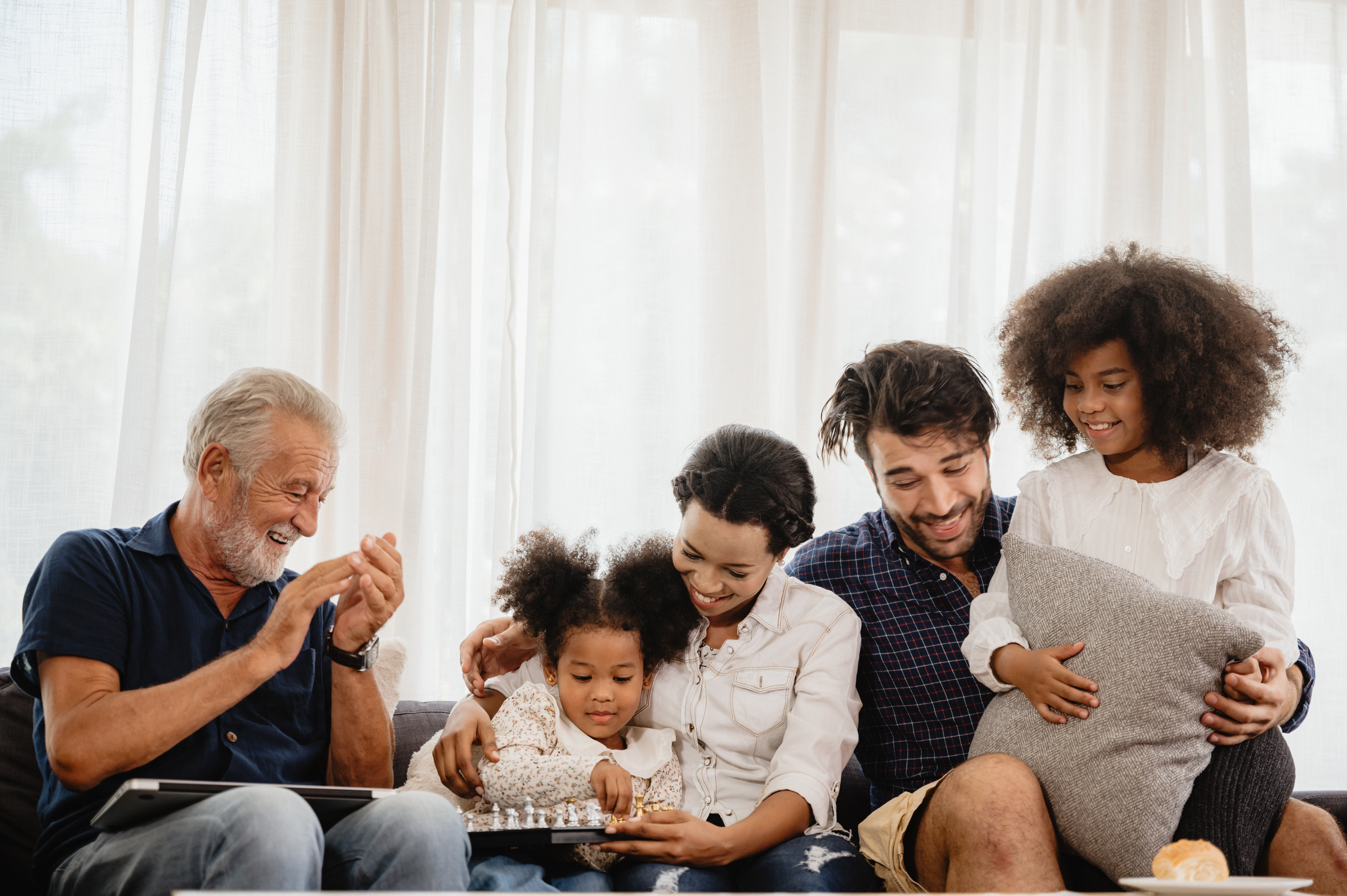 An intergenerational family is sitting on a sofa smiling and playing a board game