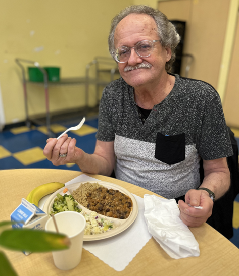 Garrett sitting at a table, smiling, with a plate of food in front of him.