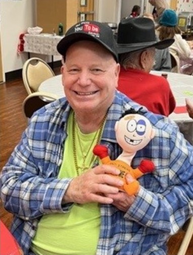 Martin Rizkowsky wearing a hat smiles while holding a stuffed animal close to his chest.