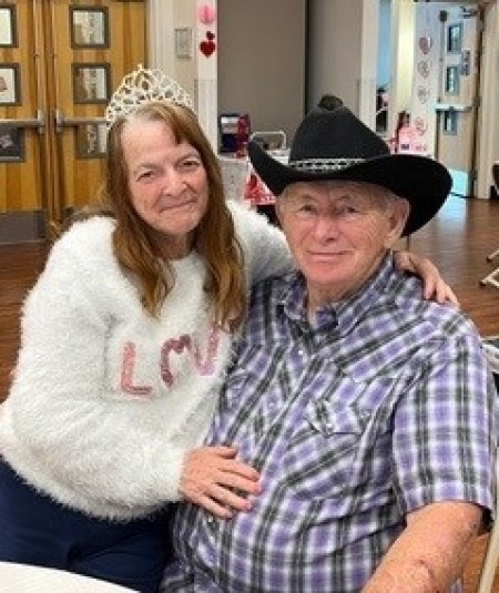 Mary and Wayne smiles while posing for a photo at a table, showcasing their affection and joy in a warm setting.
