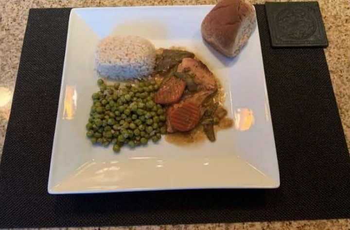 A dish with cooked meat, bright green peas, and a side of bread, all artfully displayed on a white plate.