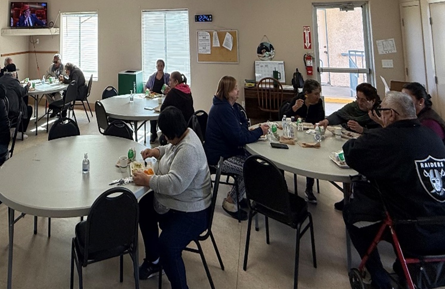 A group of people dining at tables in a well-lit room, engaged in conversation and enjoying their meals together.