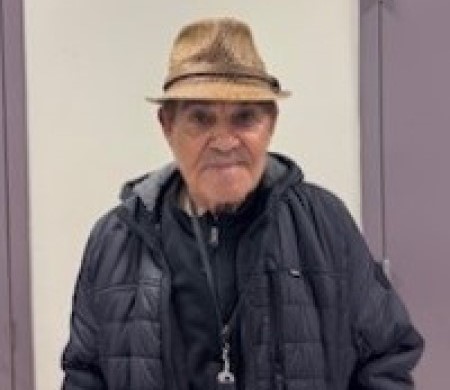 Mario Diaz in a hat and jacket stands confidently in front of a closed door.