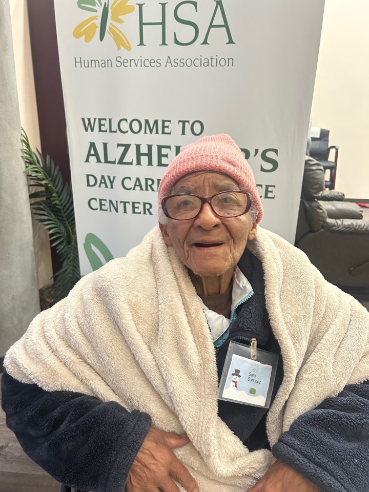 Sara in a wheelchair, snugly wrapped in a blanket, appears peaceful and reflective in her surroundings.