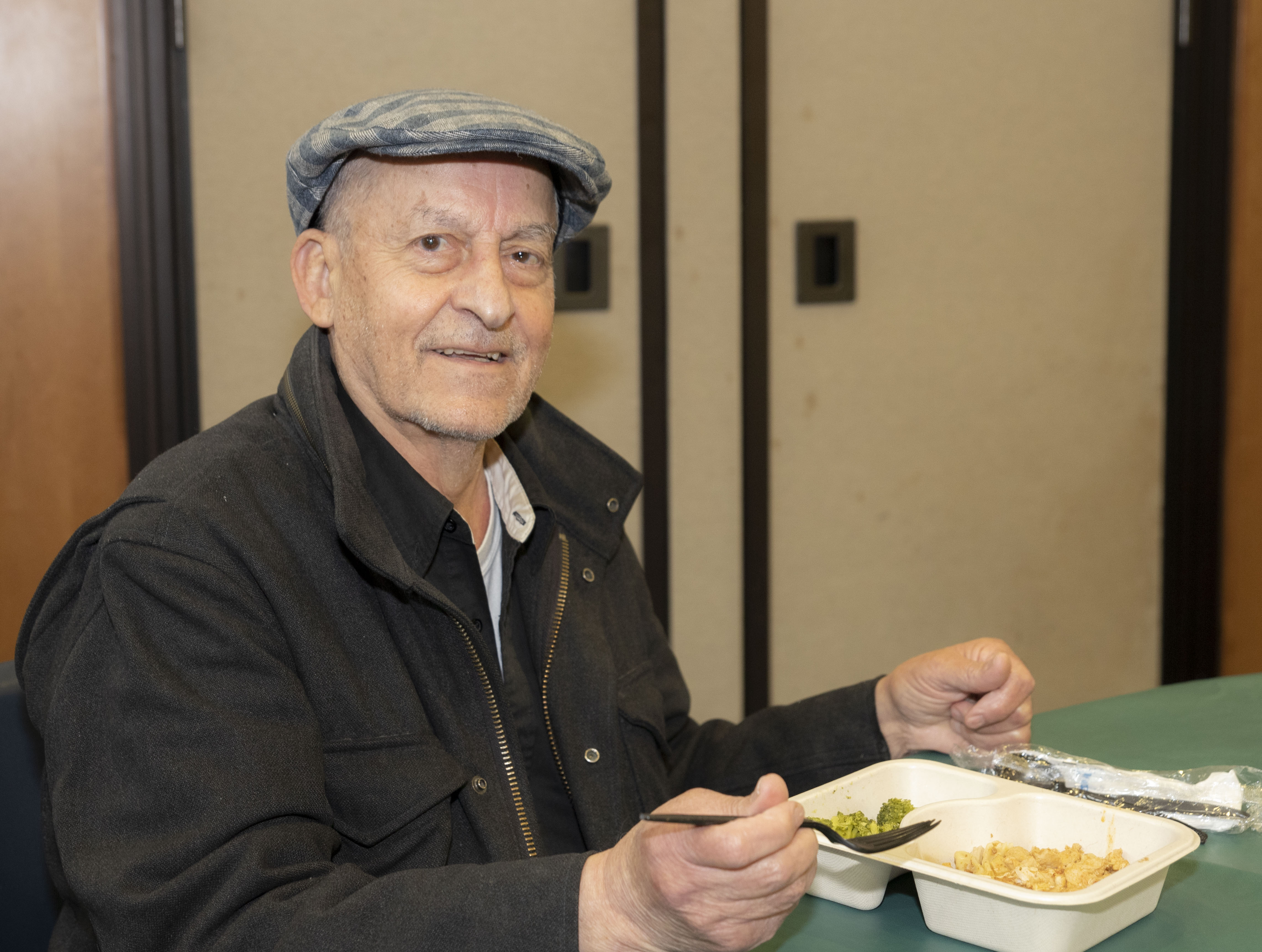 Man in cap, dark work jacket eating meal