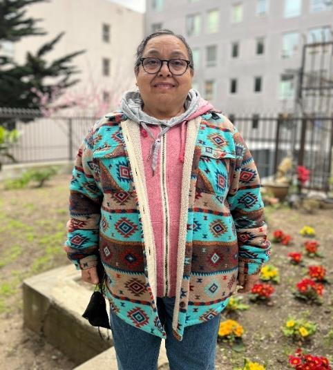 Smiling woman with pulled back hair in patterned cardigan standing in front of a flower bed