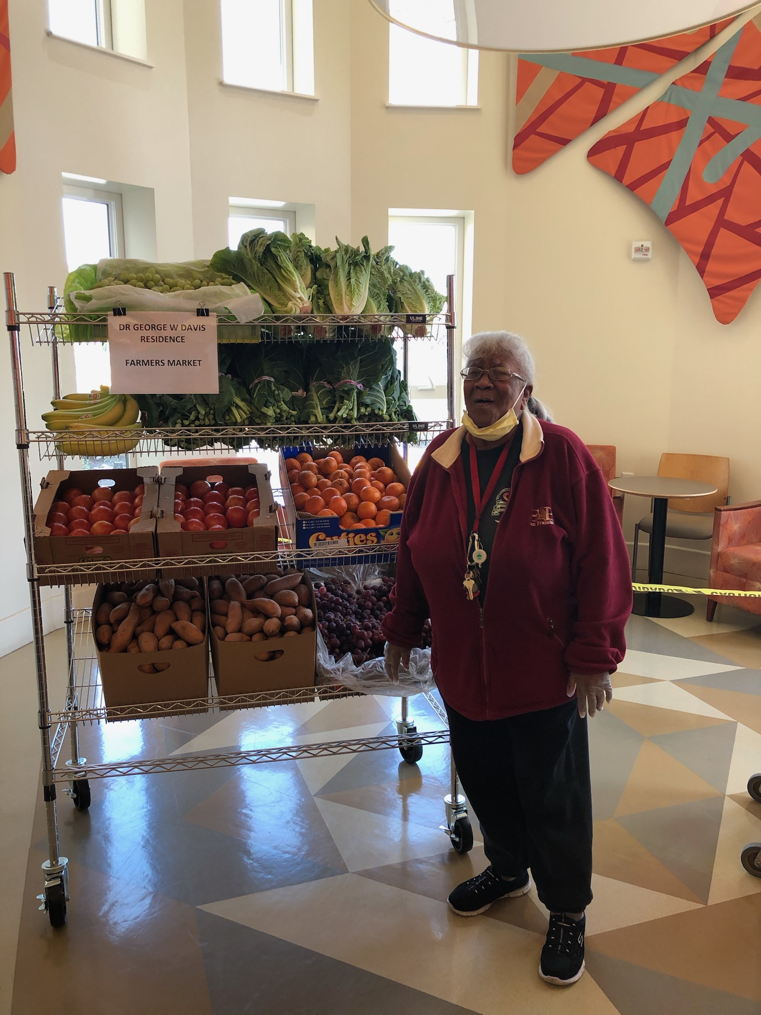 Older adult woman standing next to a shelf full of fresh fruit and vegetables.