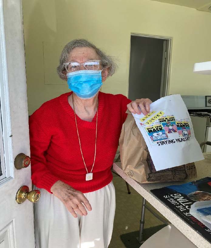 Older adult woman in red shirt and a mask receiving her home delivered meal
